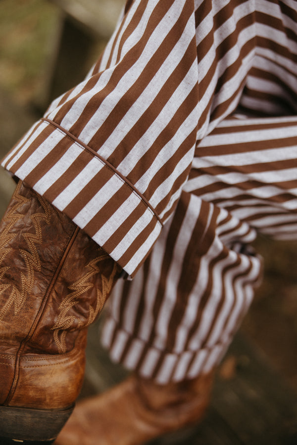 Woman wearing a striped brown and grey pants, standing against a rustic wooden background