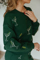 The design is embroidered on the dark green sweatshirt and sweatpants, creating a visually appealing contrast.